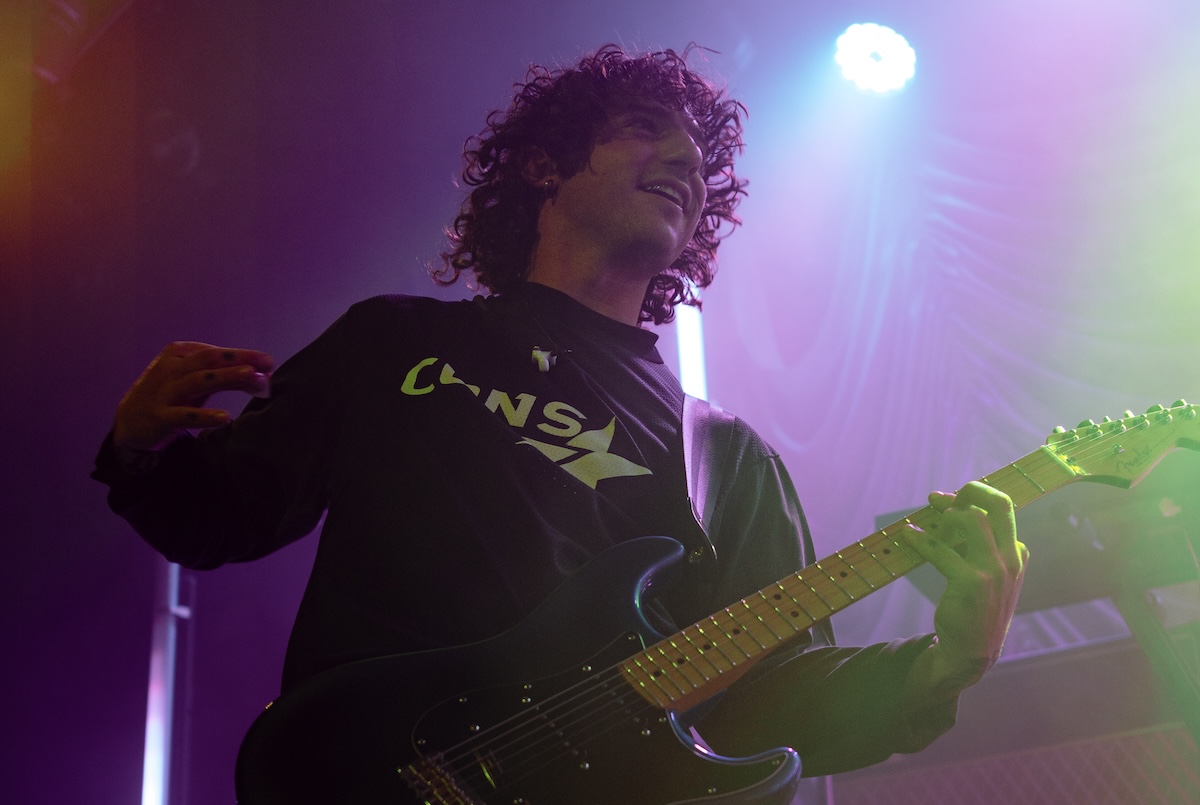 Ben Hodge of Australian indie-rock band DICE performs live on stage, playing an electric guitar under vibrant purple and green stage lights.